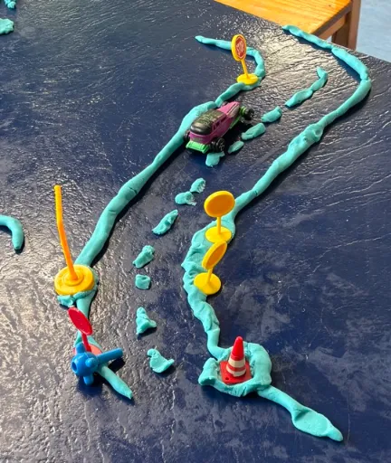 A child rolling playdough into a road at the activity table