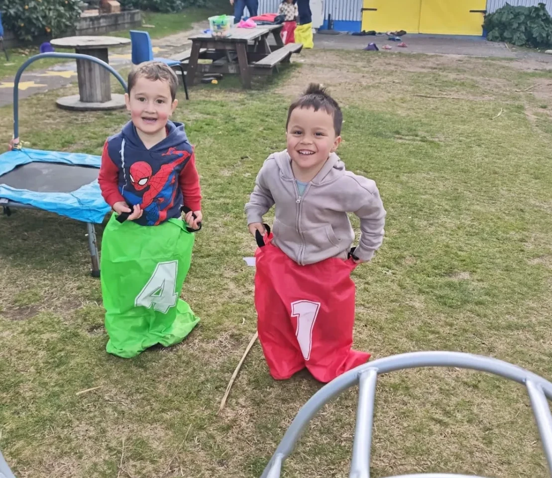 Two tamariki grinning during a sack race on the lawn at Little Darlings Childcare in Rotorua