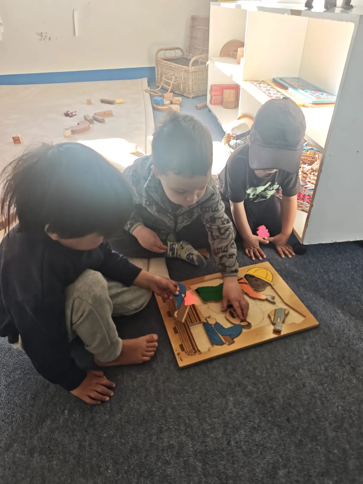 Three tamariki working together on a wooden floor puzzle