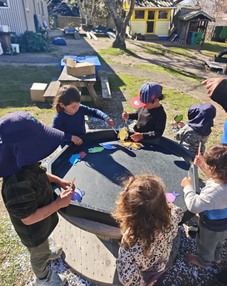 A group of tamariki playing a magnetic fishing game in the water tray outside