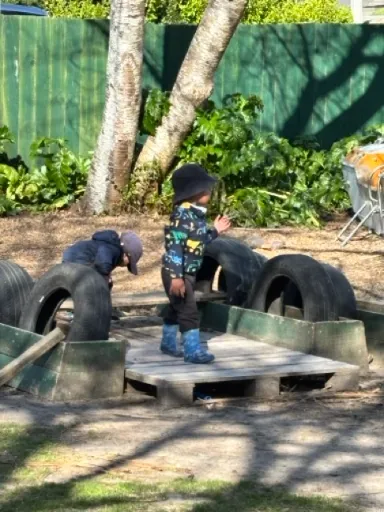 Tamariki balancing across a tyre and timber obstacle course under the trees at Little Darlings Childcare in Rotorua