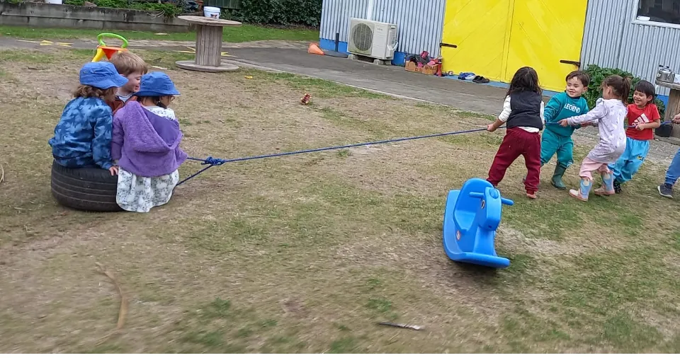 A group of tamariki pulling their friends along on a rope together on the lawn