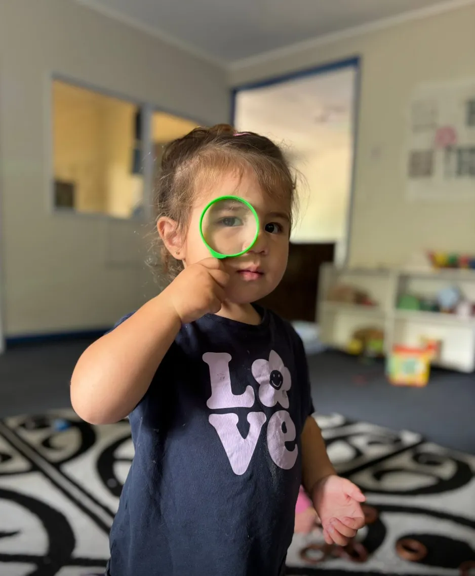 A tamaiti peering through a magnifying glass in the playroom